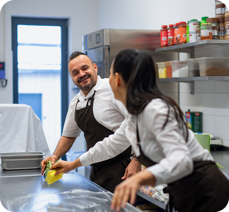 Two kitchen workers cleaning a prep station and smiling – hourly kitchen cleaning and teamwork roles through Ponte